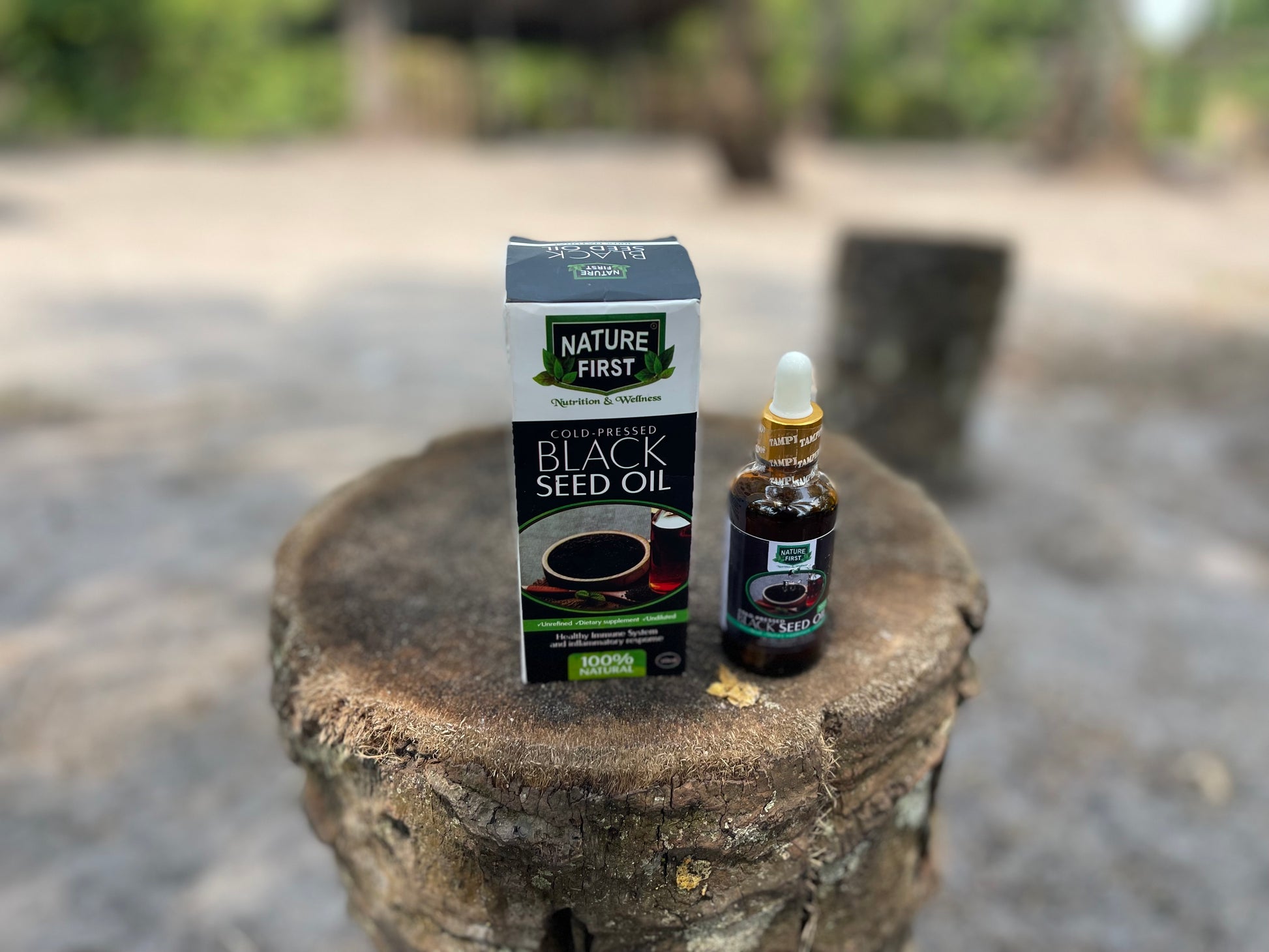 Nature First Black Seed Oil packaging and bottle on a stone surface with a blurred outdoor background
